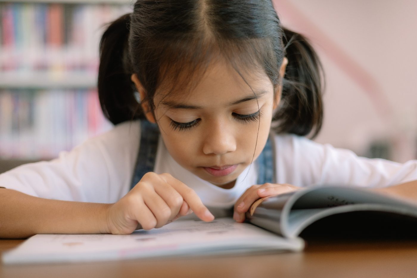 A young girl reading calmly, tracking the words with her finger.
